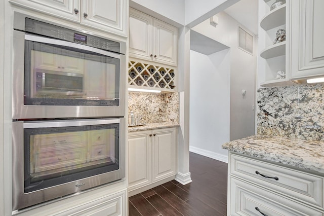 kitchen with backsplash, light stone counters, stainless steel double oven, and dark hardwood / wood-style floors