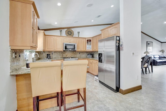 kitchen featuring kitchen peninsula, lofted ceiling, light brown cabinetry, a breakfast bar, and appliances with stainless steel finishes