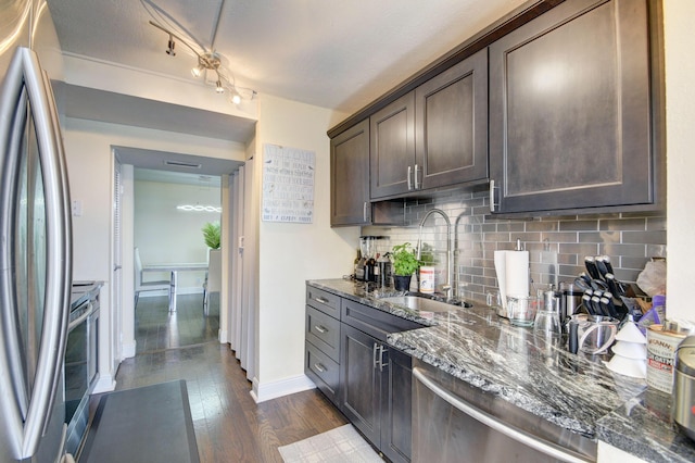 kitchen with sink, stainless steel appliances, dark hardwood / wood-style floors, dark stone countertops, and dark brown cabinets