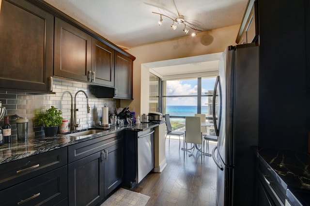 kitchen with dark brown cabinetry, sink, stainless steel appliances, dark stone counters, and a water view