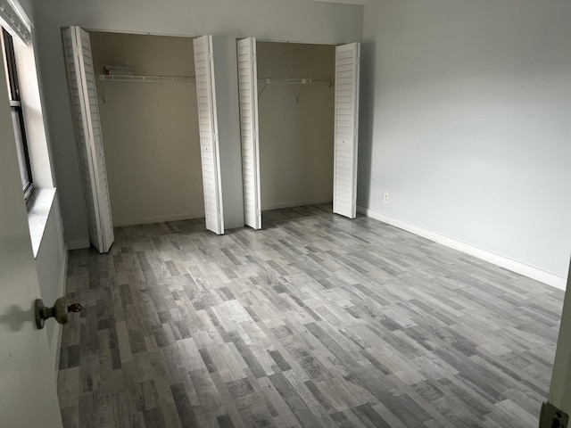 unfurnished bedroom with two closets, light hardwood / wood-style floors, and multiple windows