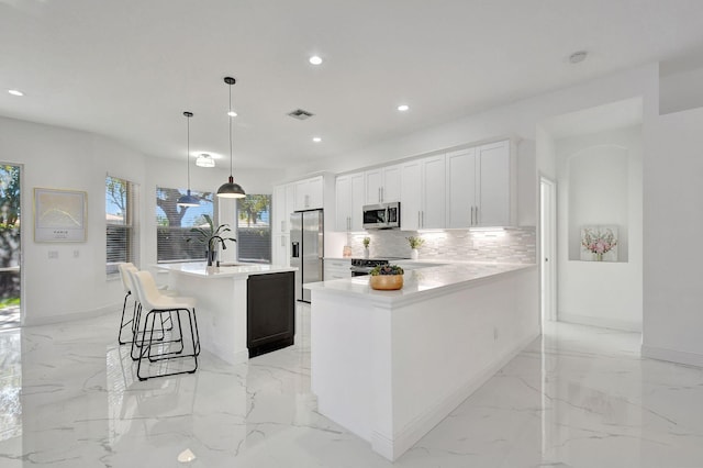 kitchen featuring appliances with stainless steel finishes, backsplash, pendant lighting, white cabinetry, and an island with sink