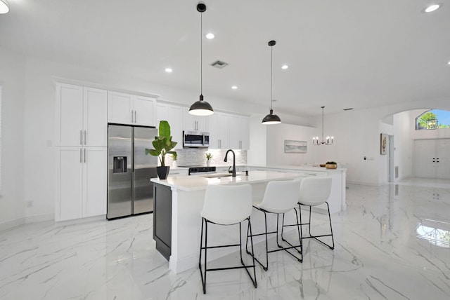 kitchen with sink, stainless steel appliances, an island with sink, decorative light fixtures, and white cabinets