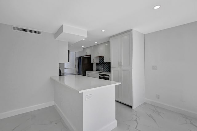 kitchen featuring dishwasher, sink, kitchen peninsula, stainless steel fridge, and white cabinetry