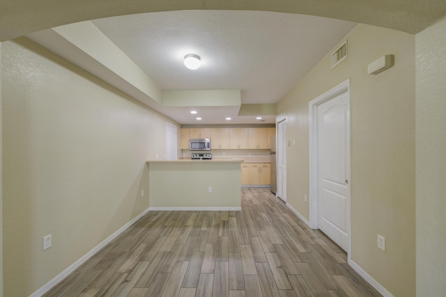 kitchen featuring light wood-type flooring, kitchen peninsula, stainless steel appliances, and light brown cabinetry