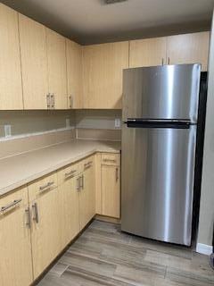 kitchen with light brown cabinets, light hardwood / wood-style floors, and stainless steel refrigerator