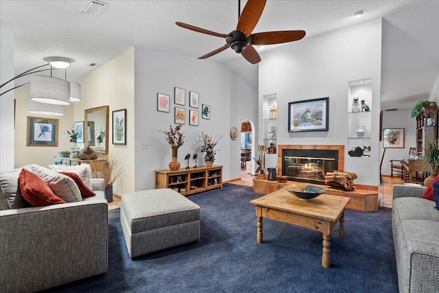 living room with carpet flooring, a textured ceiling, ceiling fan, built in features, and a fireplace