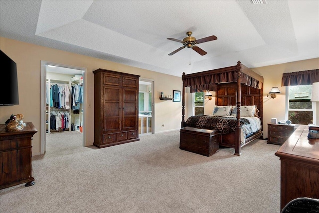 bedroom featuring light colored carpet, a closet, ceiling fan, a spacious closet, and a tray ceiling