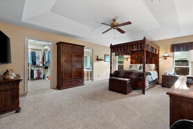 carpeted bedroom with a walk in closet, a textured ceiling, a tray ceiling, ceiling fan, and a closet