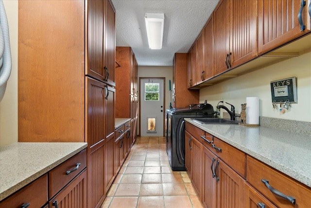 laundry room with a sink, cabinet space, light tile patterned floors, separate washer and dryer, and a textured ceiling