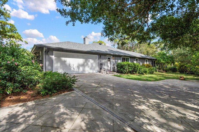 ranch-style home featuring a front yard, a garage, board and batten siding, a chimney, and concrete driveway