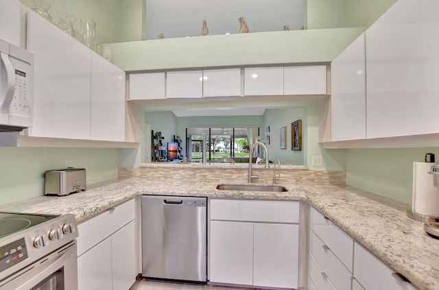 kitchen featuring white cabinets, appliances with stainless steel finishes, light stone counters, and sink