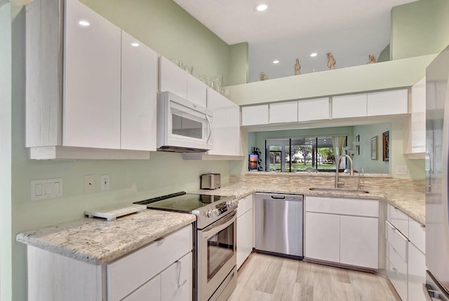 kitchen with sink, appliances with stainless steel finishes, white cabinetry, light stone countertops, and light wood-type flooring