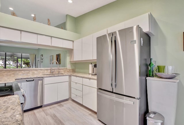 kitchen with white cabinets, sink, light hardwood / wood-style flooring, light stone counters, and stainless steel appliances