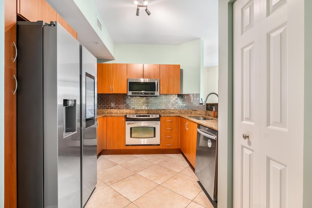 kitchen with sink, decorative backsplash, light tile patterned floors, light stone countertops, and appliances with stainless steel finishes