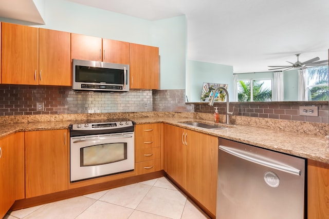 kitchen featuring light stone countertops, backsplash, stainless steel appliances, sink, and light tile patterned floors