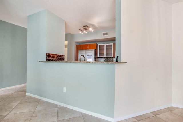 kitchen featuring kitchen peninsula, stainless steel fridge, light stone counters, and light tile patterned flooring