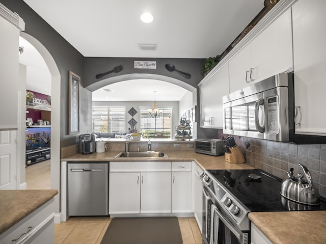 kitchen featuring appliances with stainless steel finishes, sink, light tile patterned floors, a notable chandelier, and white cabinetry