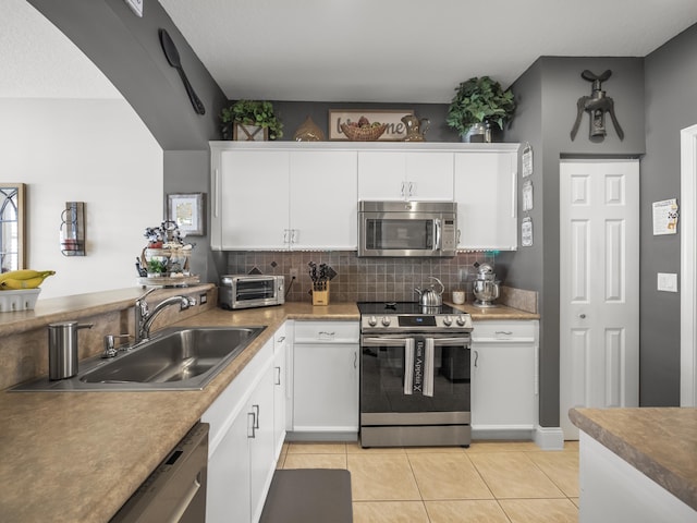 kitchen with appliances with stainless steel finishes, backsplash, sink, white cabinets, and light tile patterned flooring