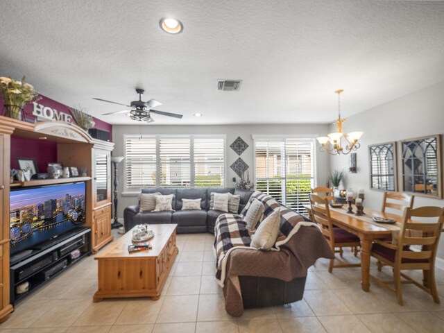 living room featuring light tile patterned floors, ceiling fan with notable chandelier, and a textured ceiling