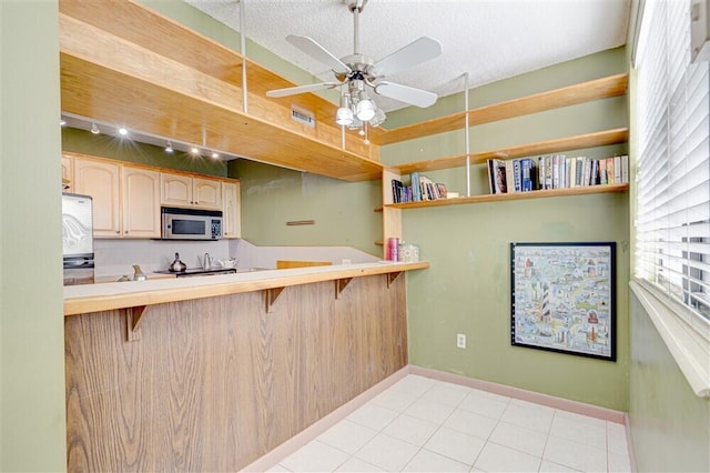 kitchen featuring a breakfast bar, ceiling fan, fridge, kitchen peninsula, and light brown cabinets