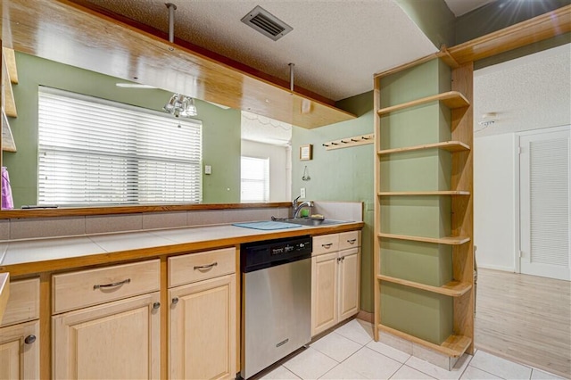 kitchen featuring sink, light tile patterned floors, stainless steel dishwasher, and a textured ceiling