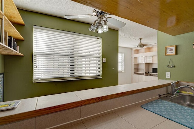 kitchen with ceiling fan, tile counters, sink, and a textured ceiling