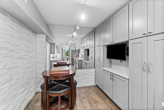 kitchen with gray cabinetry, rail lighting, light hardwood / wood-style floors, and brick wall