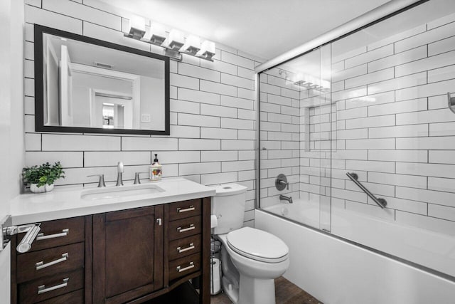 full bathroom featuring vanity, combined bath / shower with glass door, decorative backsplash, toilet, and tile walls