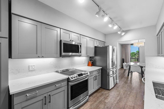 kitchen featuring appliances with stainless steel finishes, gray cabinets, light hardwood / wood-style flooring, and light stone counters