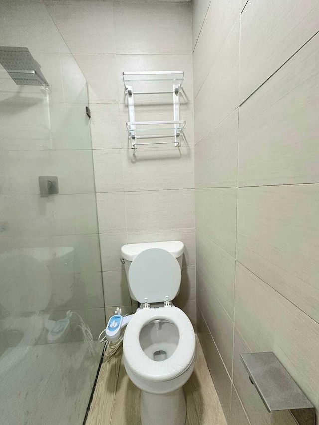 bathroom with wood-type flooring, tile walls, and toilet