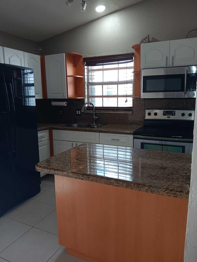 kitchen featuring appliances with stainless steel finishes, sink, light tile patterned floors, dark stone countertops, and white cabinetry