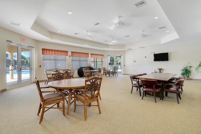 carpeted dining space with a tray ceiling and french doors