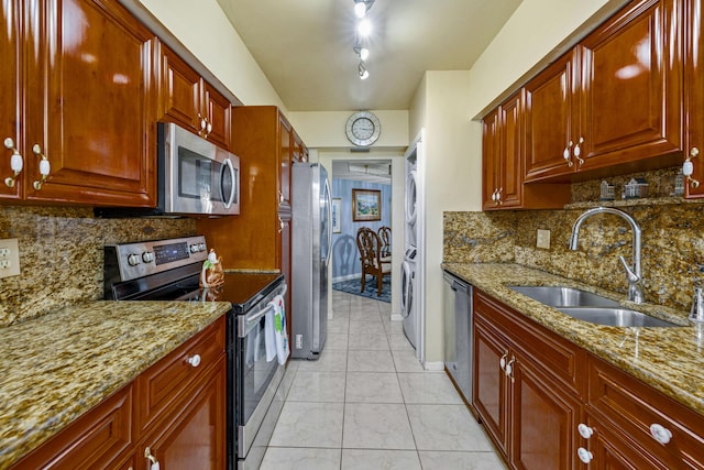 kitchen with stainless steel appliances, light stone counters, stacked washer / dryer, and sink