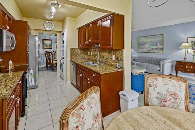 kitchen featuring light stone counters, sink, appliances with stainless steel finishes, and stacked washer and clothes dryer