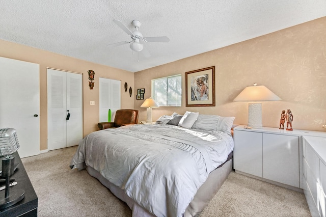 carpeted bedroom with ceiling fan, a textured ceiling, and multiple closets