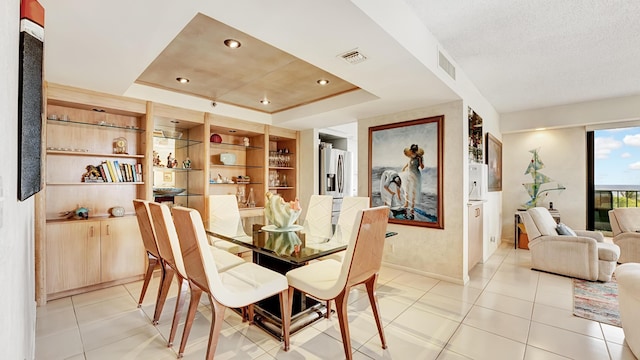 dining room with a tray ceiling, light tile patterned flooring, and a textured ceiling