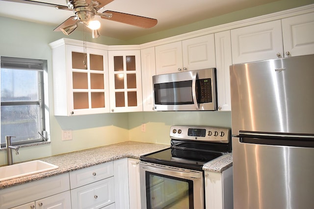 kitchen with appliances with stainless steel finishes, light stone counters, ceiling fan, sink, and white cabinets