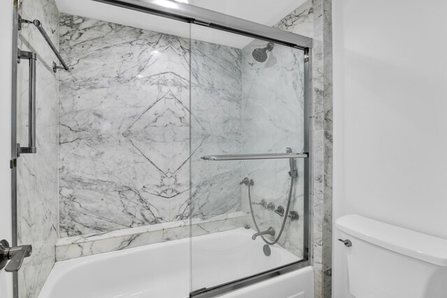 bathroom featuring toilet and bath / shower combo with glass door