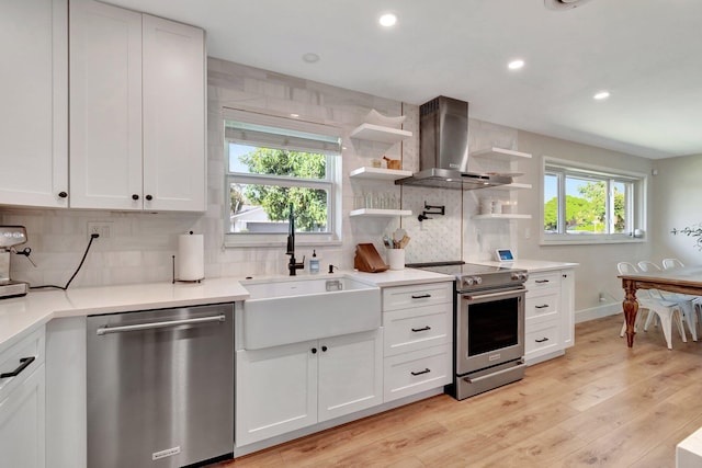 kitchen featuring stainless steel appliances, white cabinetry, wall chimney exhaust hood, and light hardwood / wood-style floors