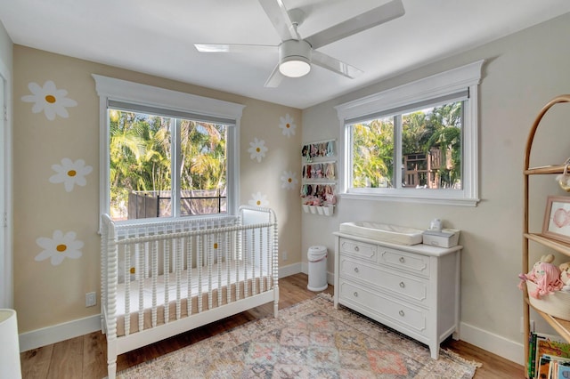 bedroom with light wood-type flooring, a nursery area, and ceiling fan