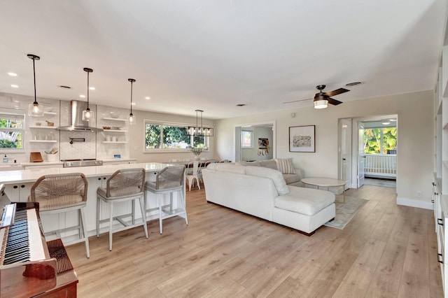 living room with ceiling fan with notable chandelier, light wood-type flooring, and a wealth of natural light