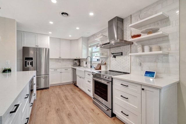 kitchen featuring backsplash, light wood-type flooring, stainless steel appliances, wall chimney range hood, and white cabinetry