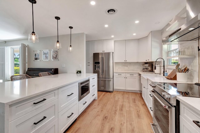 kitchen with stainless steel appliances, pendant lighting, light hardwood / wood-style flooring, white cabinetry, and range hood