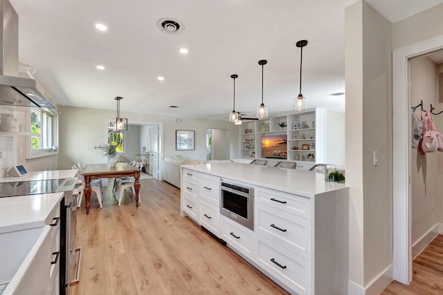 kitchen featuring pendant lighting, wall chimney exhaust hood, light hardwood / wood-style floors, white cabinetry, and stainless steel appliances