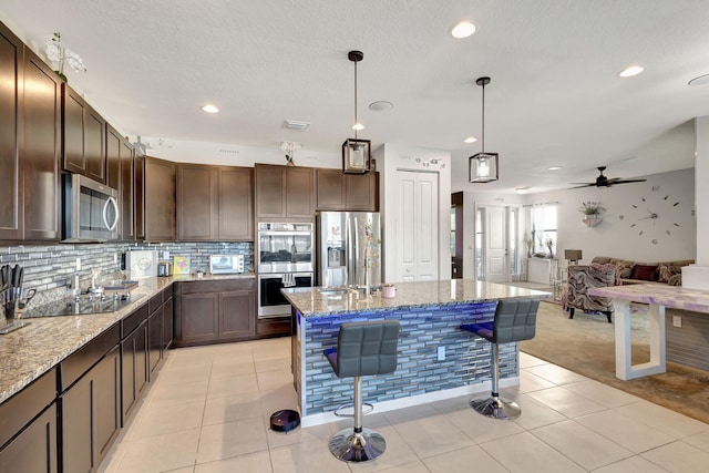 kitchen featuring dark brown cabinetry, light stone counters, stainless steel appliances, and decorative light fixtures