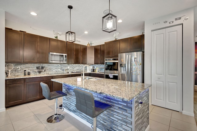 kitchen featuring a center island with sink, hanging light fixtures, sink, light stone countertops, and appliances with stainless steel finishes