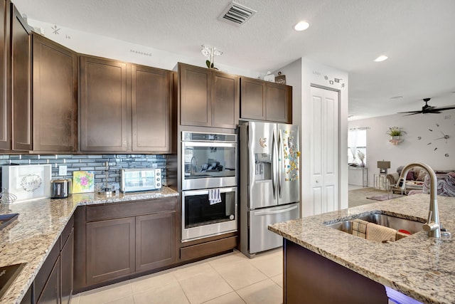 kitchen featuring appliances with stainless steel finishes, backsplash, light stone counters, dark brown cabinetry, and sink