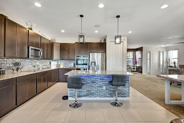 kitchen with light stone countertops, appliances with stainless steel finishes, a kitchen island with sink, hanging light fixtures, and a breakfast bar area