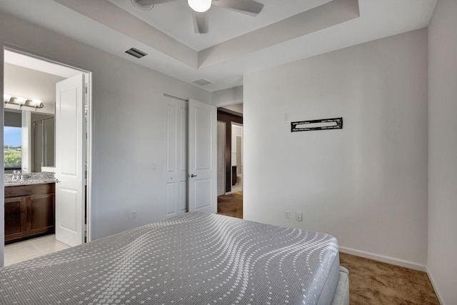 bedroom with light carpet, a tray ceiling, ceiling fan, connected bathroom, and a closet